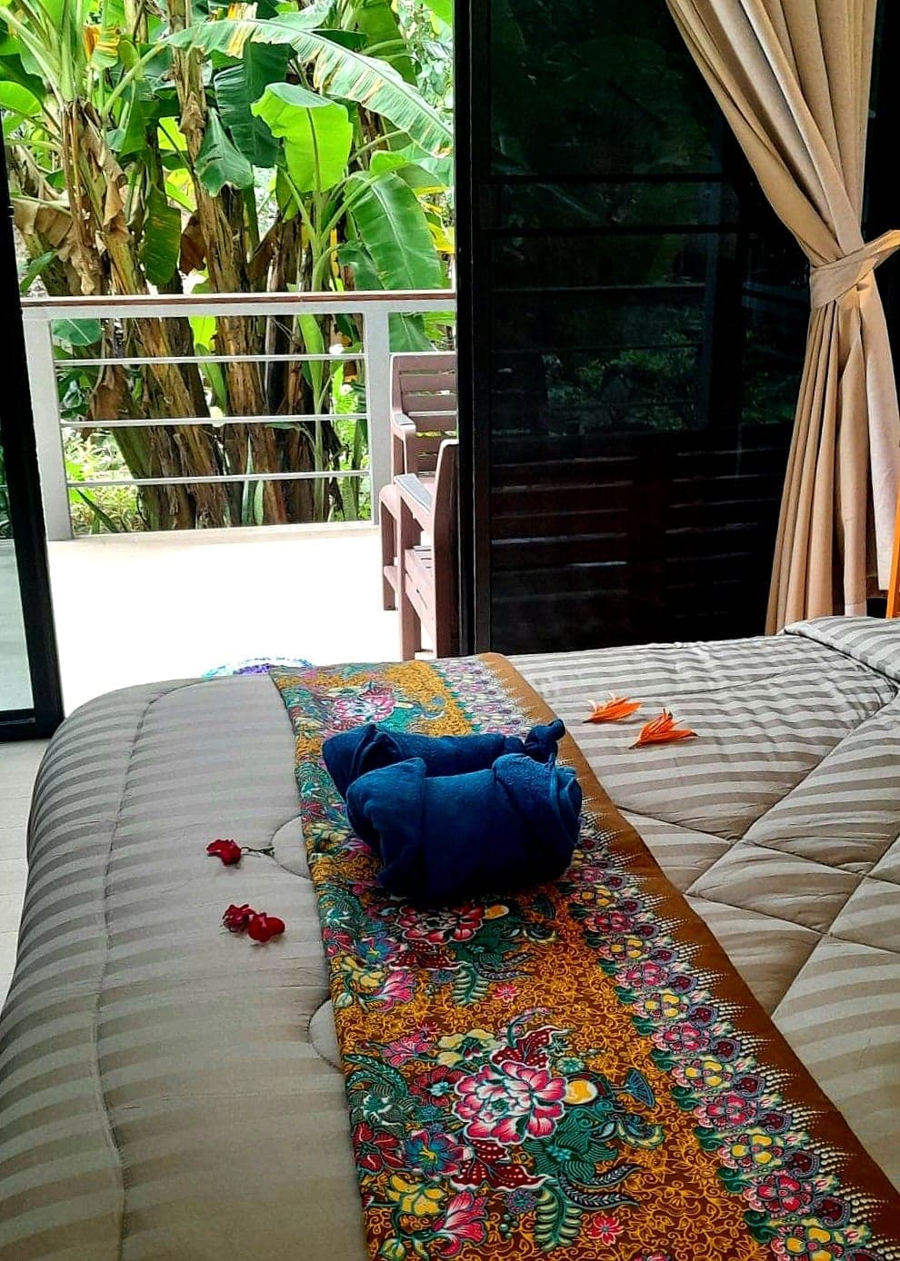 Towels folded into a swan on a batik runner, the balcony doors open onto the banana grove