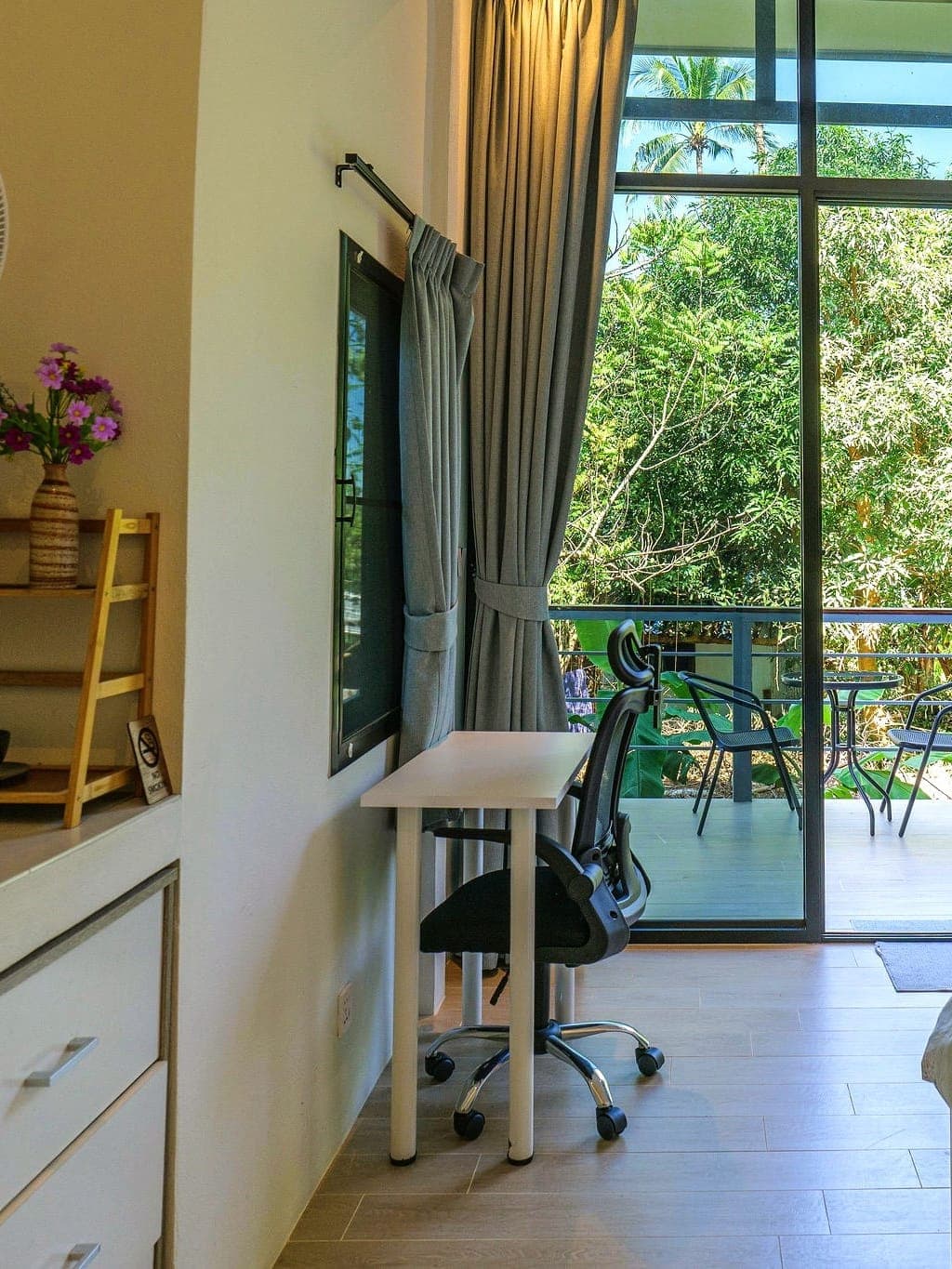 Modern Bungalow 2 — desk with an ergonomic office chair, wall television and full-height doors onto the balcony with a table and chairs