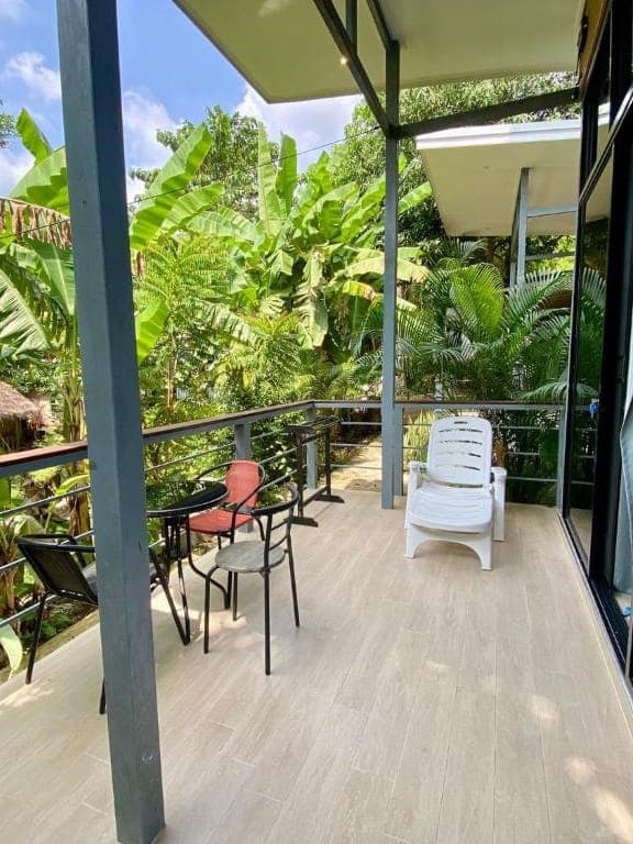 Modern Bungalow 2 — tiled private balcony with a round table, chairs and a lounger among the banana trees