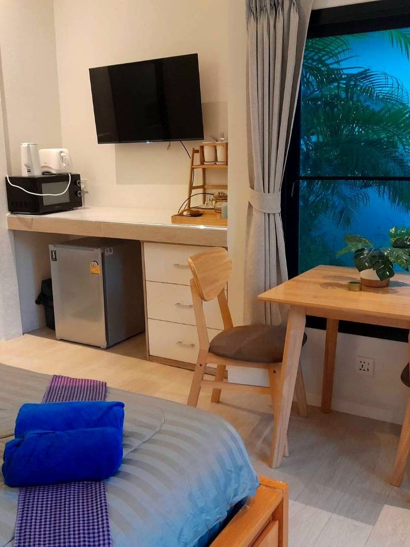 Modern Bungalow 3 – das Zimmer vom Bett aus: Küchenzeile mit Kühlschrank, Mikrowelle und Wasserkocher, der Flachbildfernseher und der Holztisch am Fenster