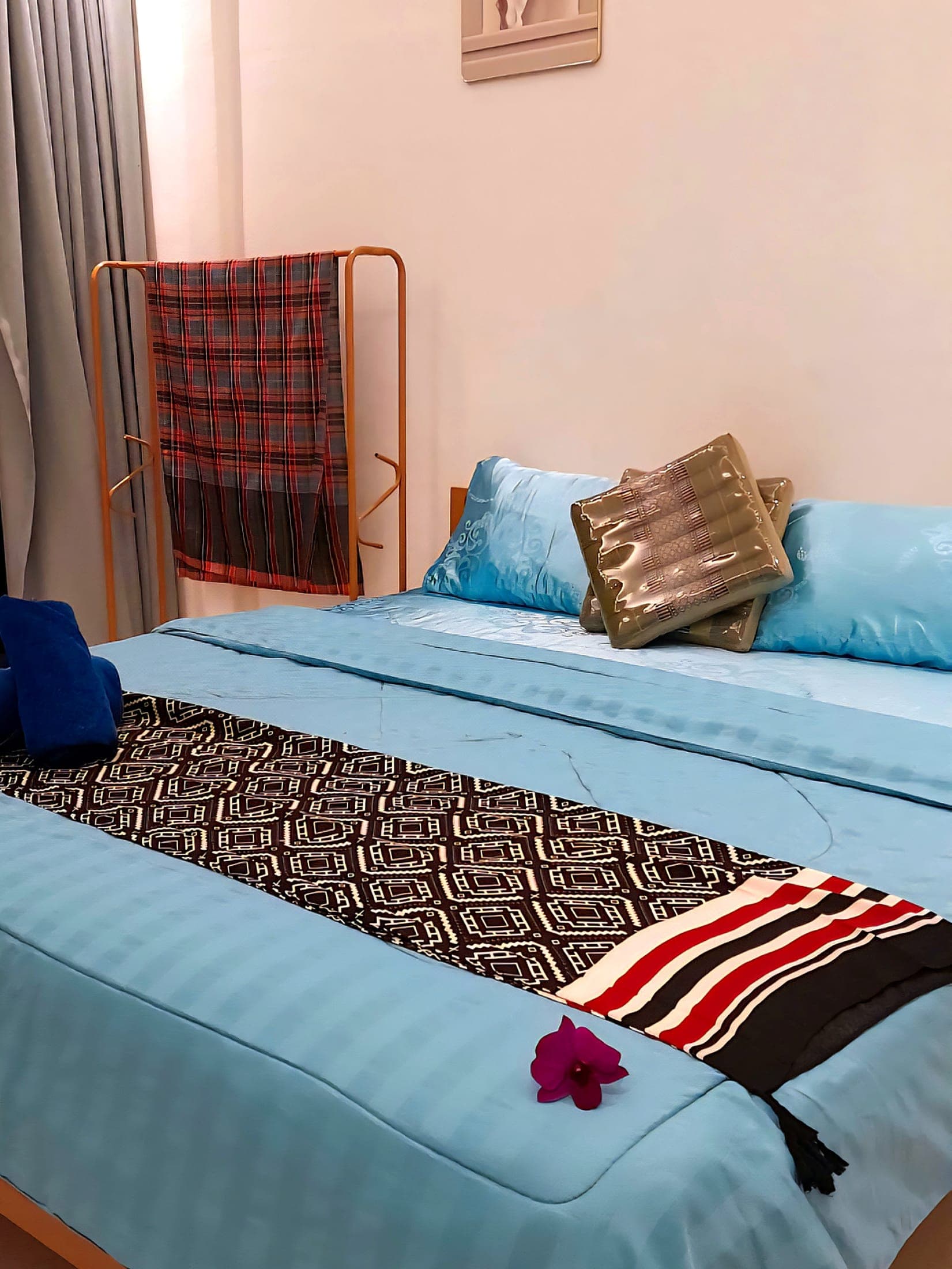 The bed made up for arrival: Thai runner, folded towels and an orchid