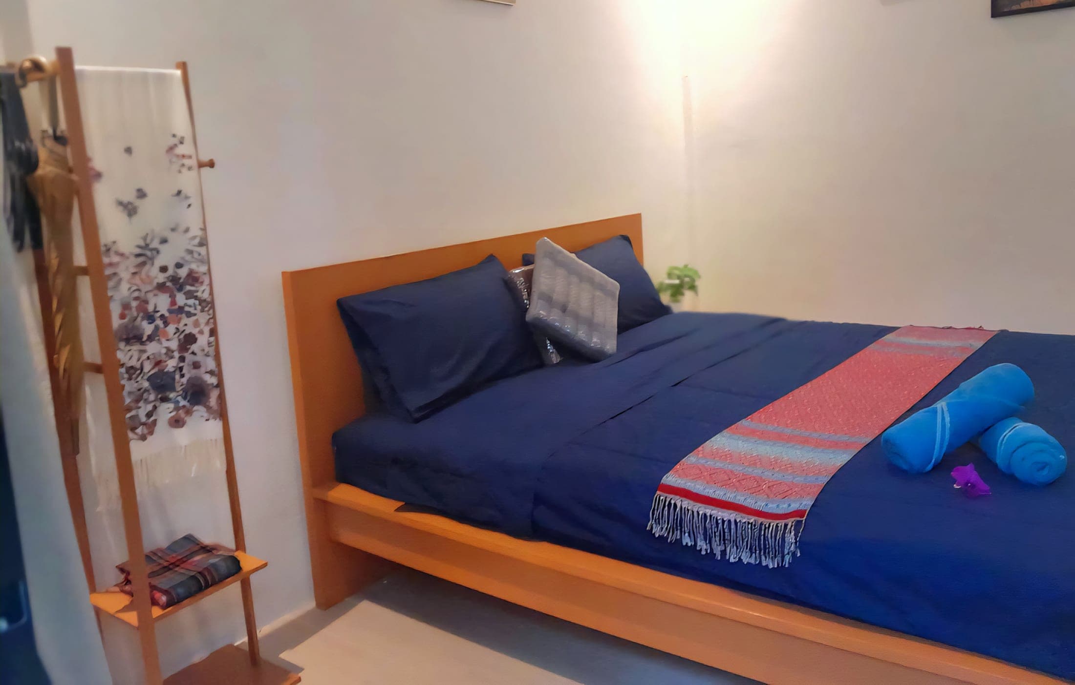 Bed dressed with a Thai runner, clothes rack and framed pictures