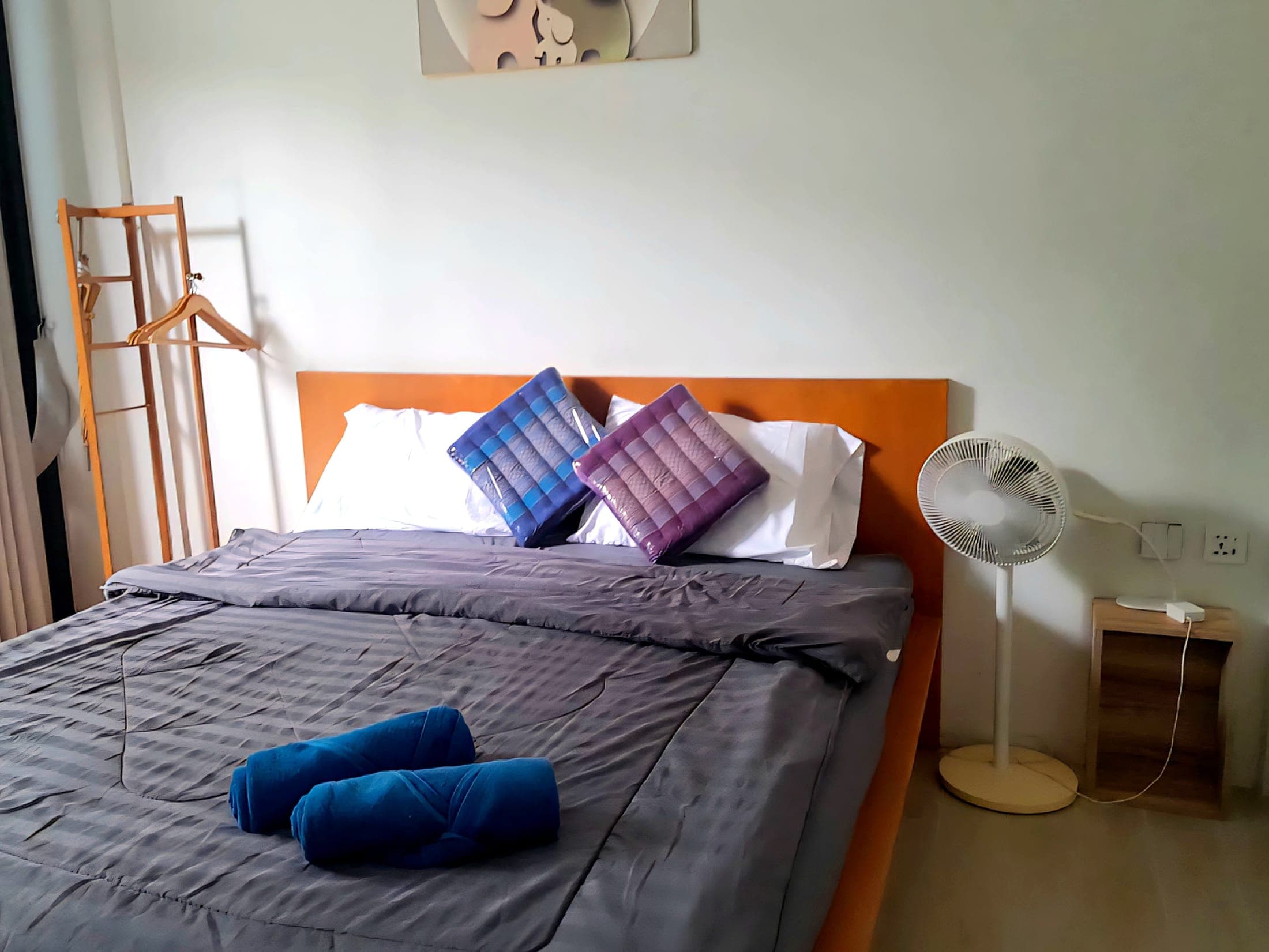 King-size bed with Thai triangle cushions, rolled towels and the floor fan